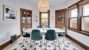 A dining room with a round table, six chairs, a hanging light fixture, wooden cabinets, and a window with a view. - Nokomis Blue (Minneapolis)