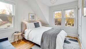 A bedroom with a bed, two bedside lamps, a framed picture on the wall, and a window with a view of trees. - Nokomis Blue (Minneapolis)