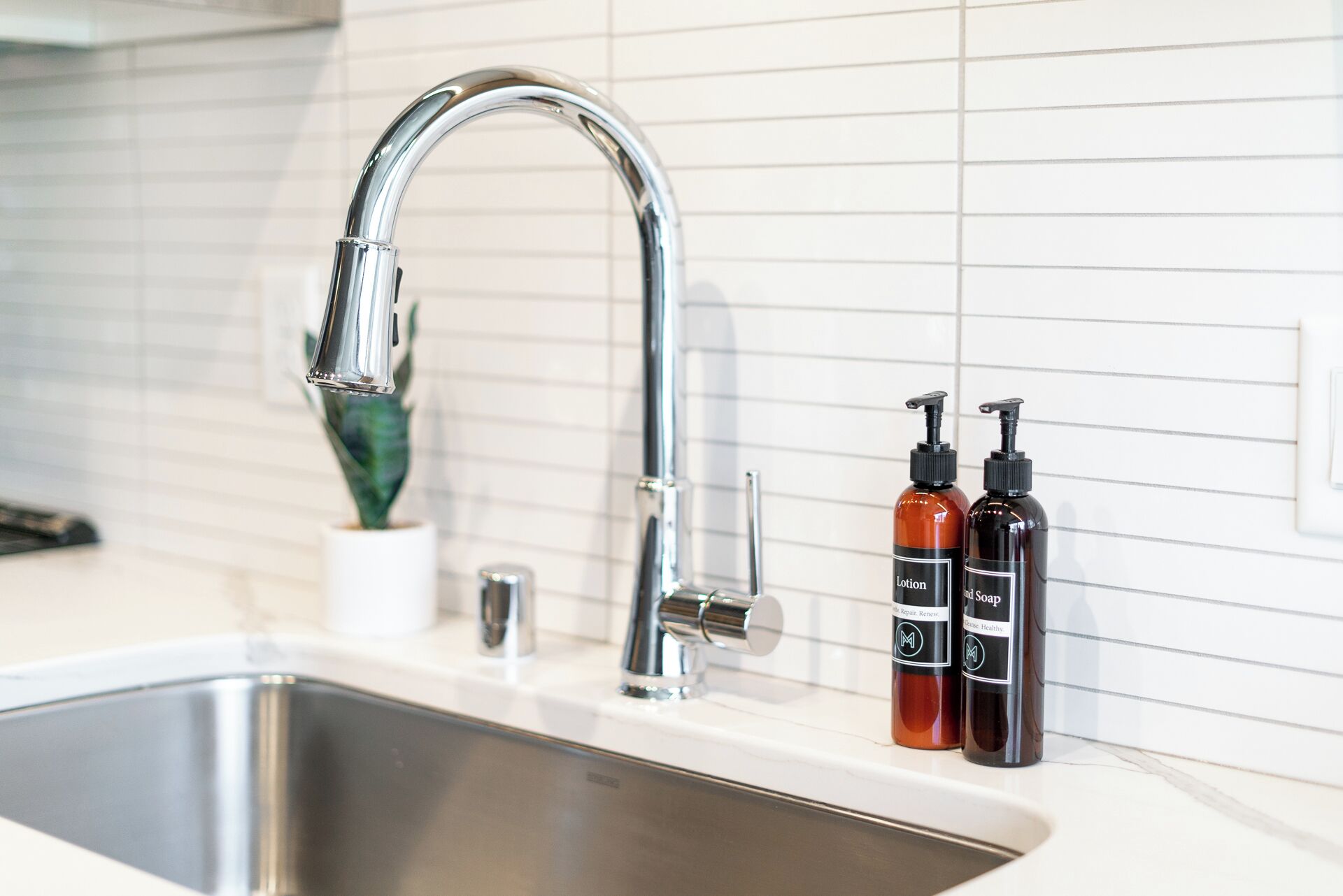 A modern kitchen sink with a chrome faucet and two soap dispensers.