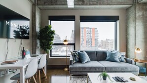 A modern living room with a grey sofa, a white coffee table, and a TV displaying 'MINNESOTA'. - Sable 401 - Studio (Minneapolis)
