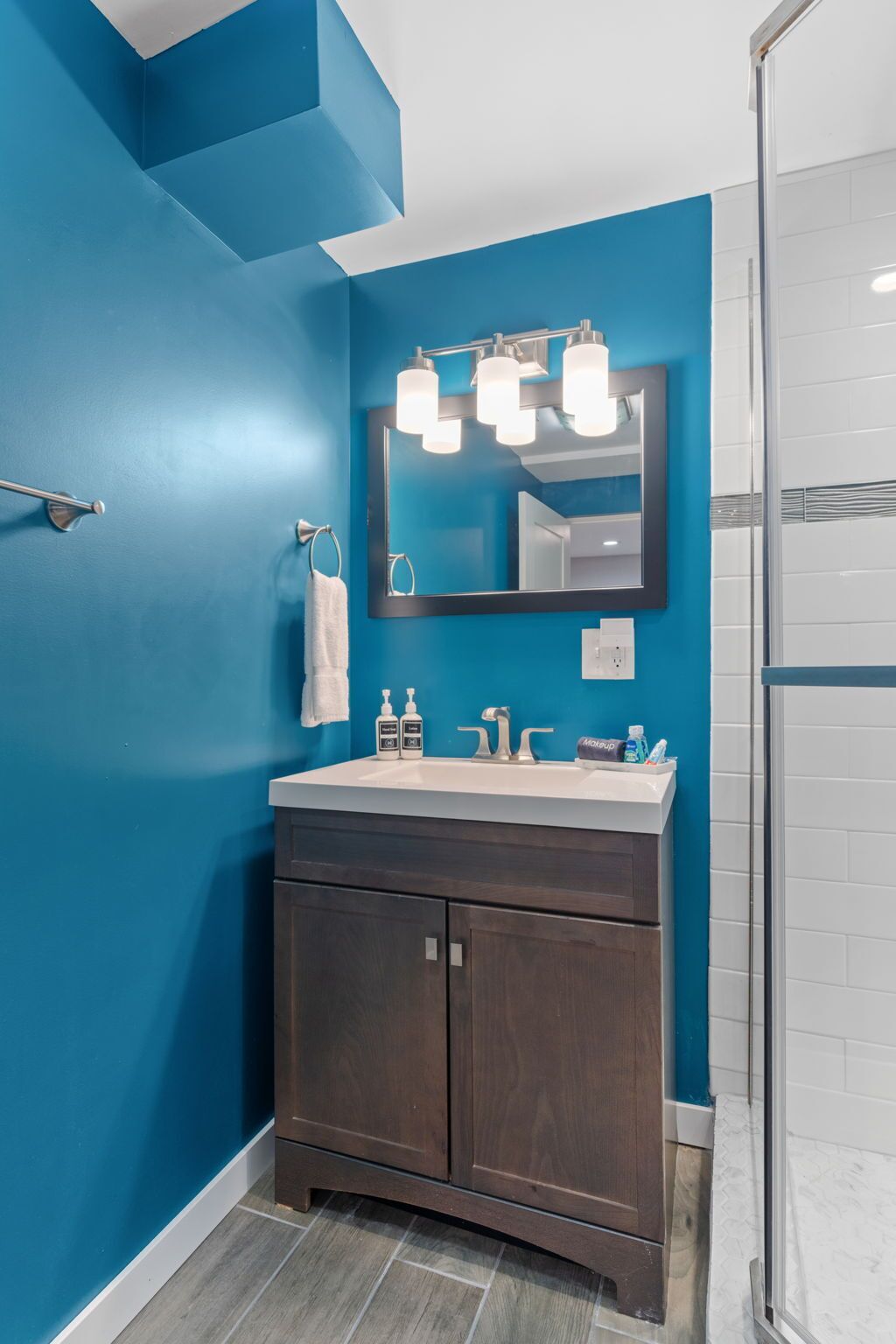 A bathroom with a blue wall, a dark wood vanity, a white sink, and a mirror with three lights.