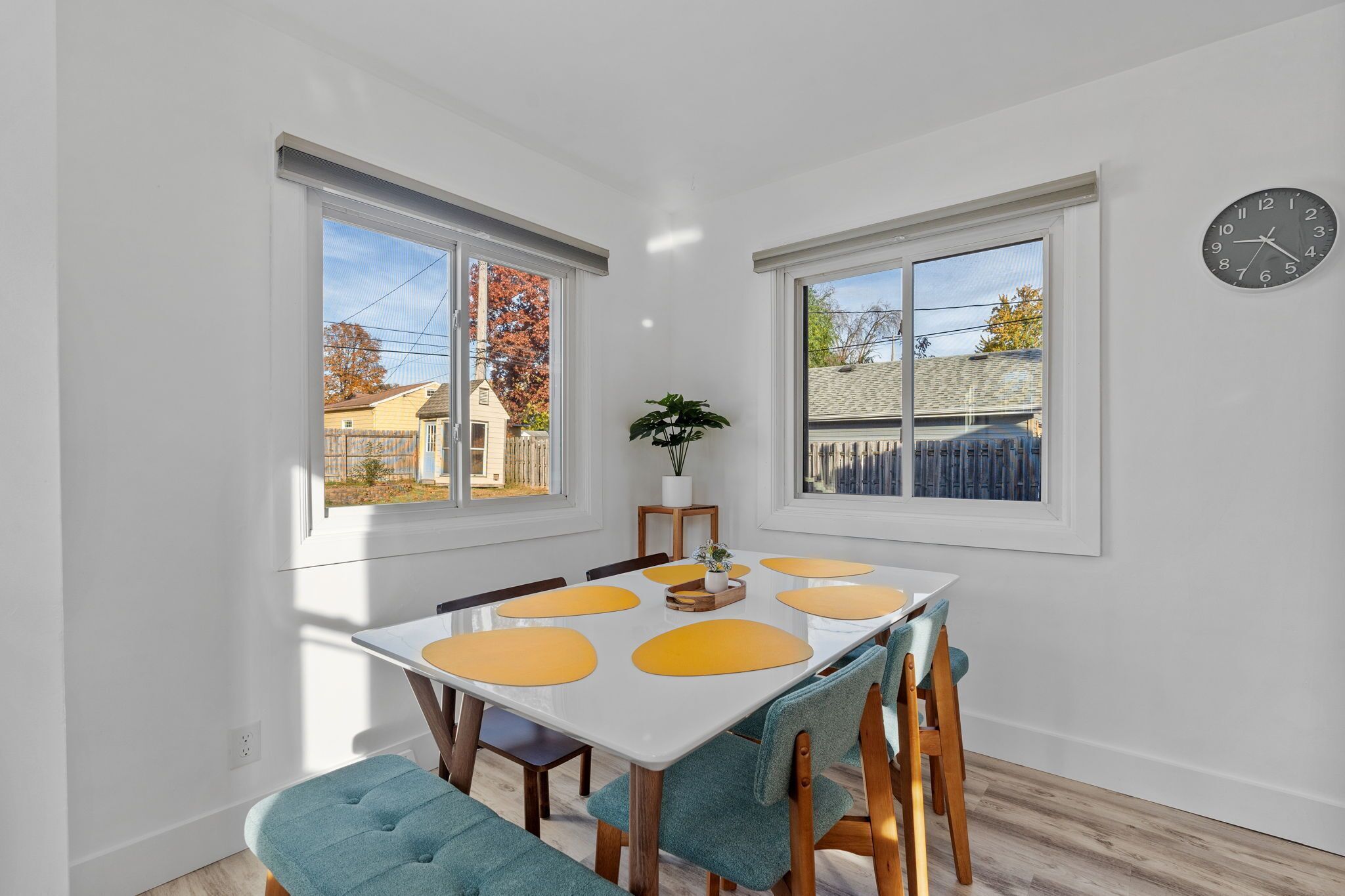 Un coin repas avec une table blanche, des sets de table jaunes et des chaises de couleur turquoise.