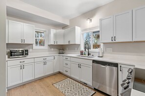 A modern kitchen with white cabinets, a dishwasher, a microwave, and a window with a view of trees. - Red Maple (Minneapolis)