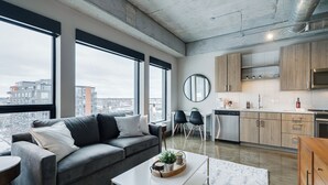 Een modern appartement met een grijze bank, een eethoek en een keuken.
