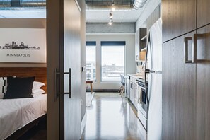 A modern hotel room with a bed, kitchenette, and large windows offering city views. - Sable 704 - One Bedroom (Minneapolis)