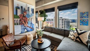 Ein modernes Wohnzimmer mit einem großen Gemälde, einem Sofa, einem Couchtisch und Blick auf die Stadt.