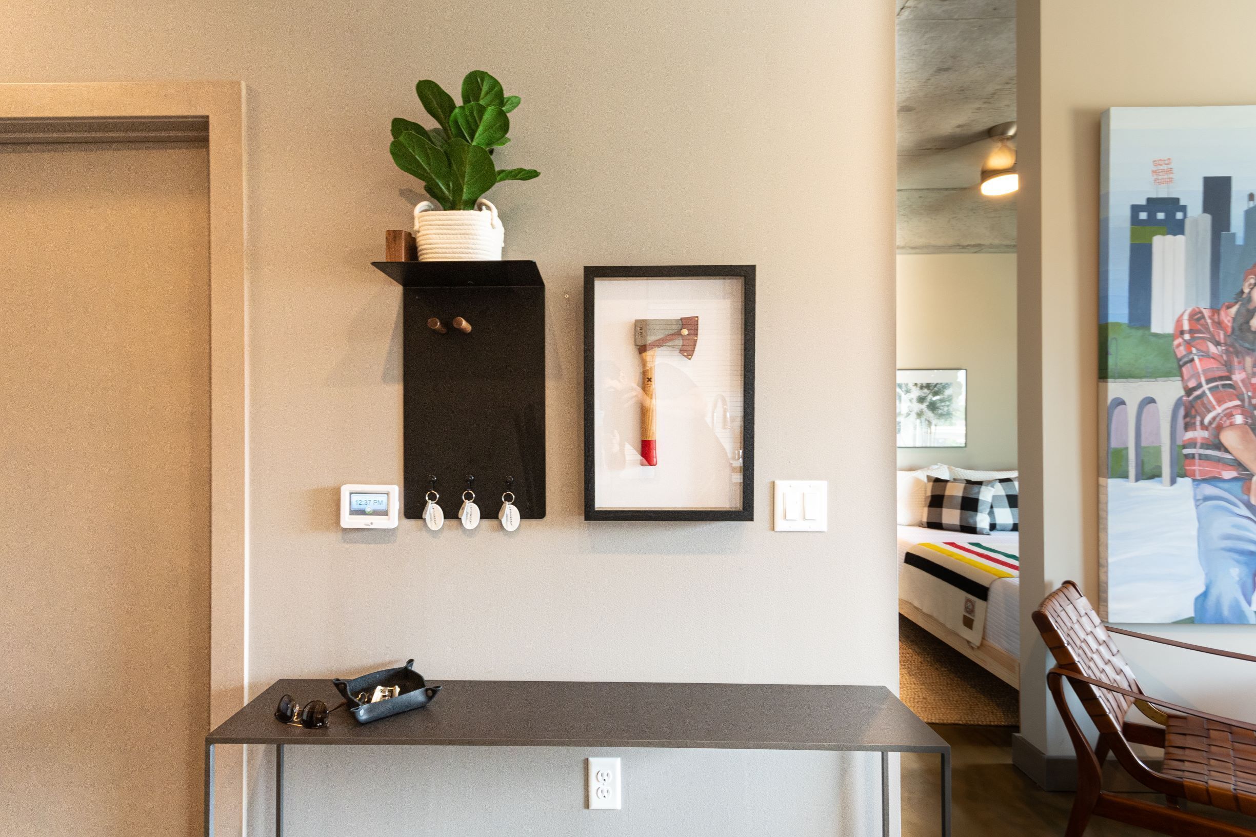 A modern hotel lobby with a reception desk, a framed artwork, a potted plant, and a bed with a colorful bedspread.
