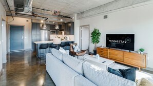 Een moderne woonkamer met een grijze bank, een houten tv-meubel en een grote flatscreen televisie waarop 'Minnestay' staat.