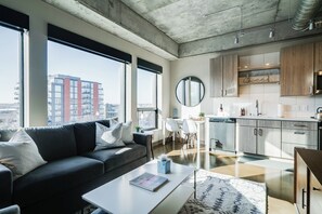 A modern apartment with a living room, kitchen, and large windows offering a city view.