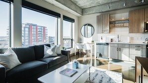 A modern apartment with a living room, kitchen, and large windows offering a city view.