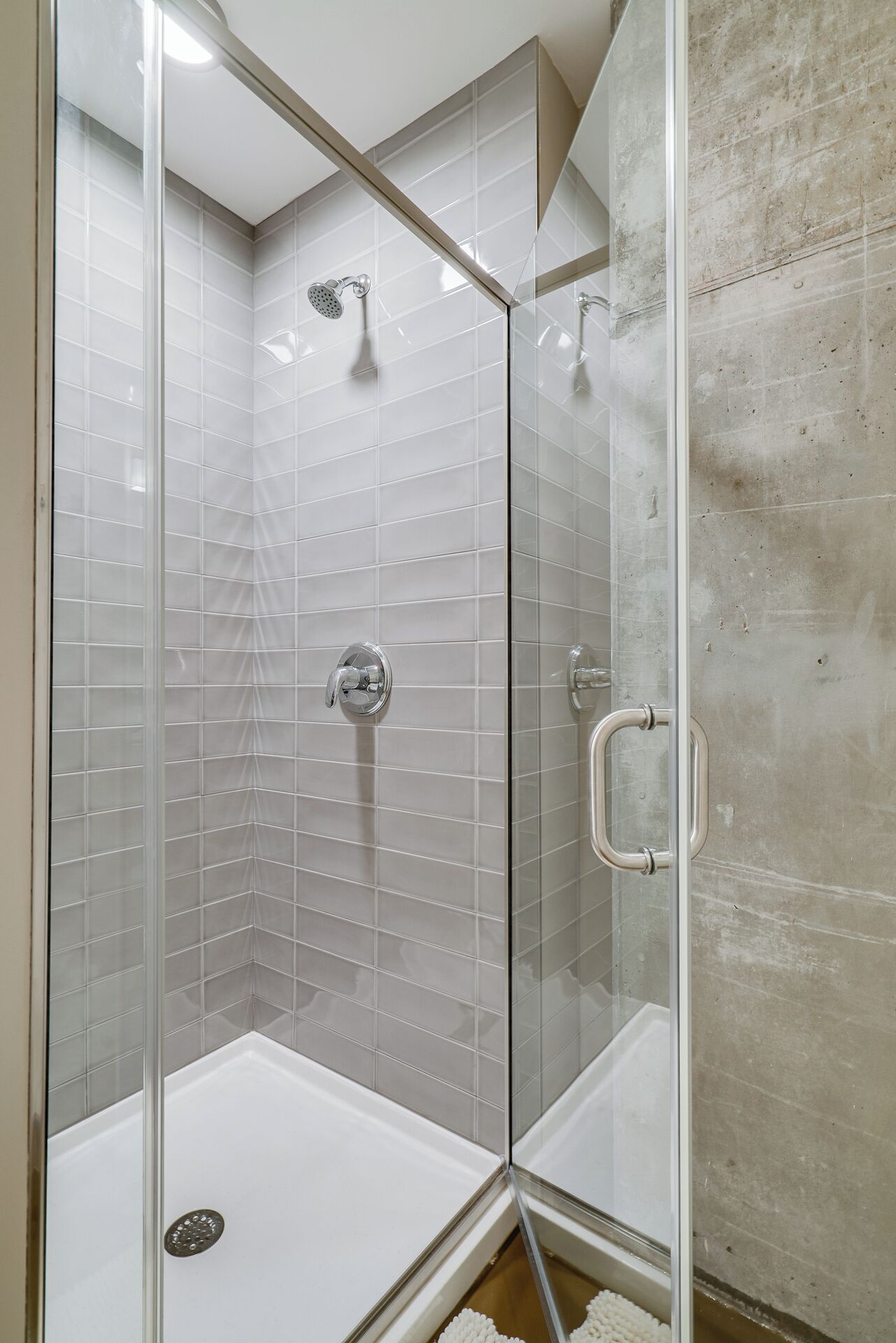A glass-enclosed shower with a white tiled wall and a concrete floor.
