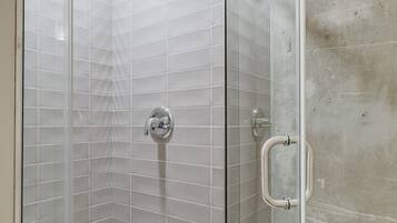 A glass-enclosed shower with a white tiled wall and a concrete floor.