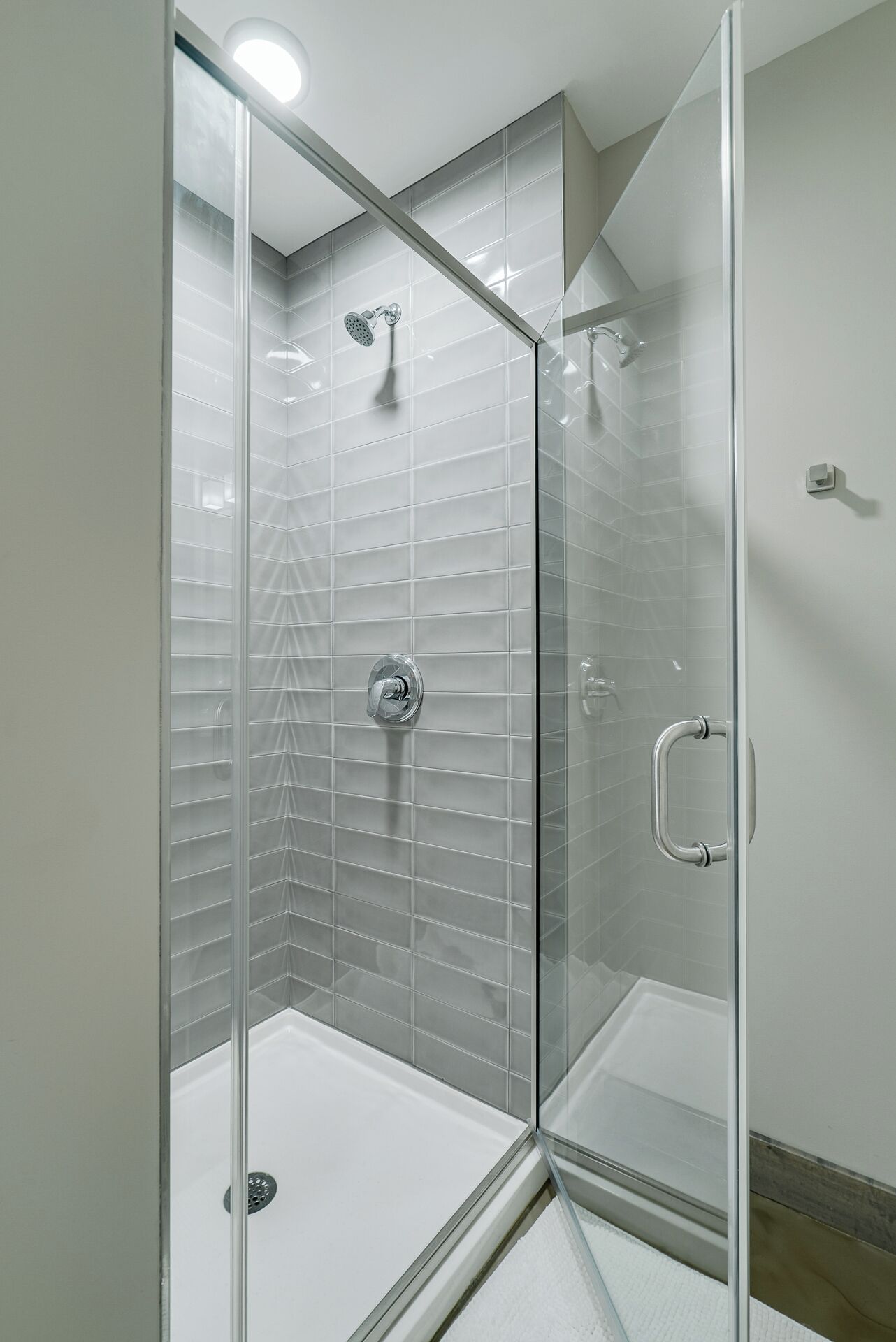 Een douche met glazen wand, betegelde muur en een witte vloer.