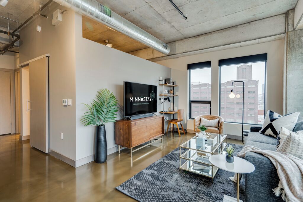 A modern living room with a large flat-screen TV, a sofa, a coffee table, and a large window with a city view.
