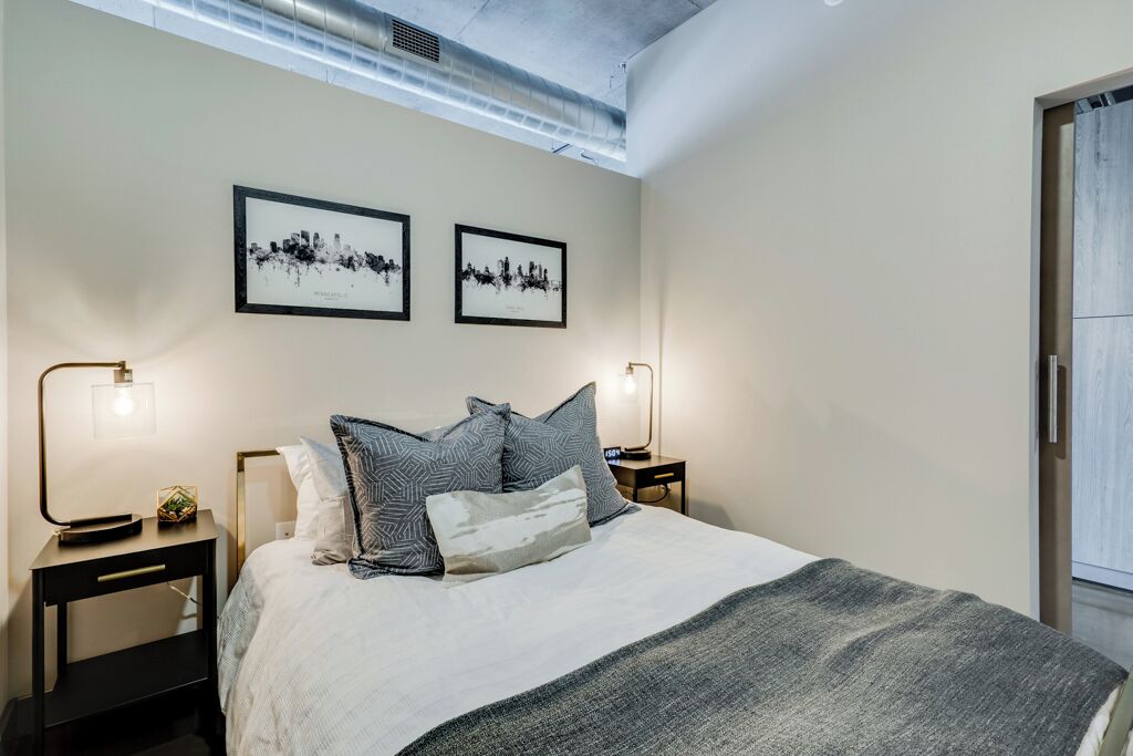 A modern bedroom with a large bed, two framed cityscape pictures on the wall, and bedside lamps.