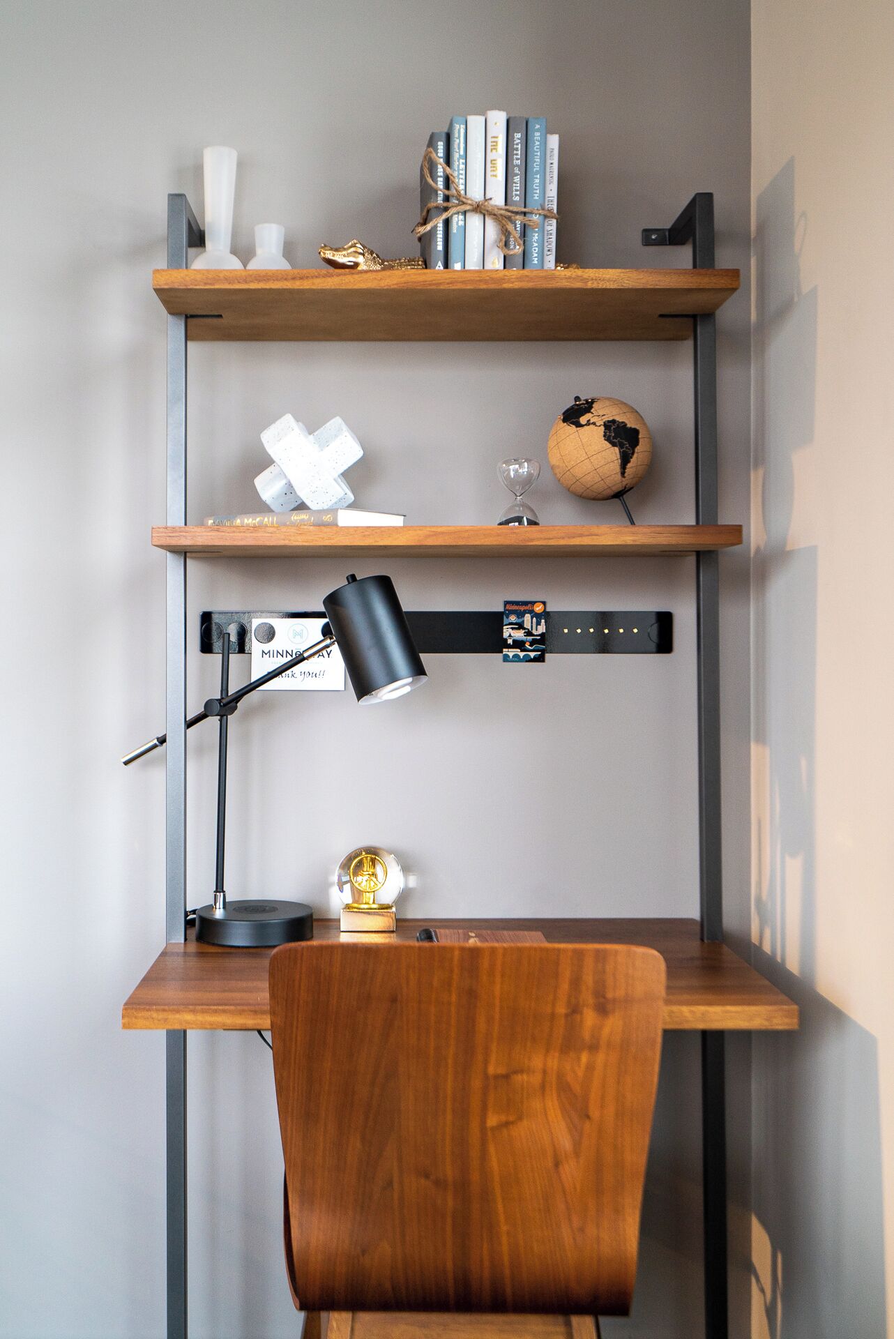 Un bureau en bois, sur lequel se trouvent une lampe noire, un globe terrestre et des livres rangés sur des étagères.