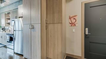 A modern kitchen with light wood cabinets, stainless steel appliances, and a dark door.