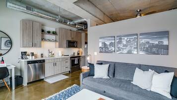 Een moderne woonruimte met een keuken, een grijze bank met gestreepte kussens en stadsgezicht kunst aan de muur.