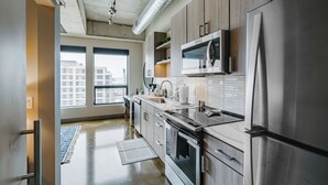A modern kitchen with stainless steel appliances, wooden cabinets, and a large window providing a view of the city. - Sable 606 - One Bedroom (Minneapolis)