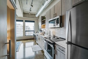 A modern kitchen with stainless steel appliances, wooden cabinets, and a large window providing a view of the city. - Sable 606 - One Bedroom (Minneapolis)