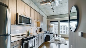 A modern kitchen with stainless steel appliances, wooden cabinets, and a large window offering a city view. - Sable 607 - Alcove (Minneapolis)