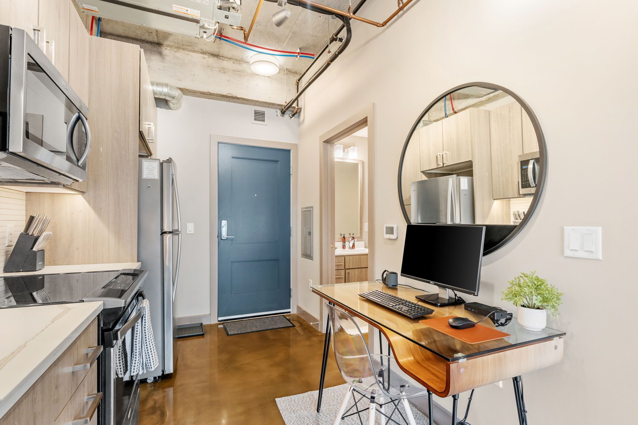 A modern kitchen with stainless steel appliances, a blue door, and a round mirror on the wall.