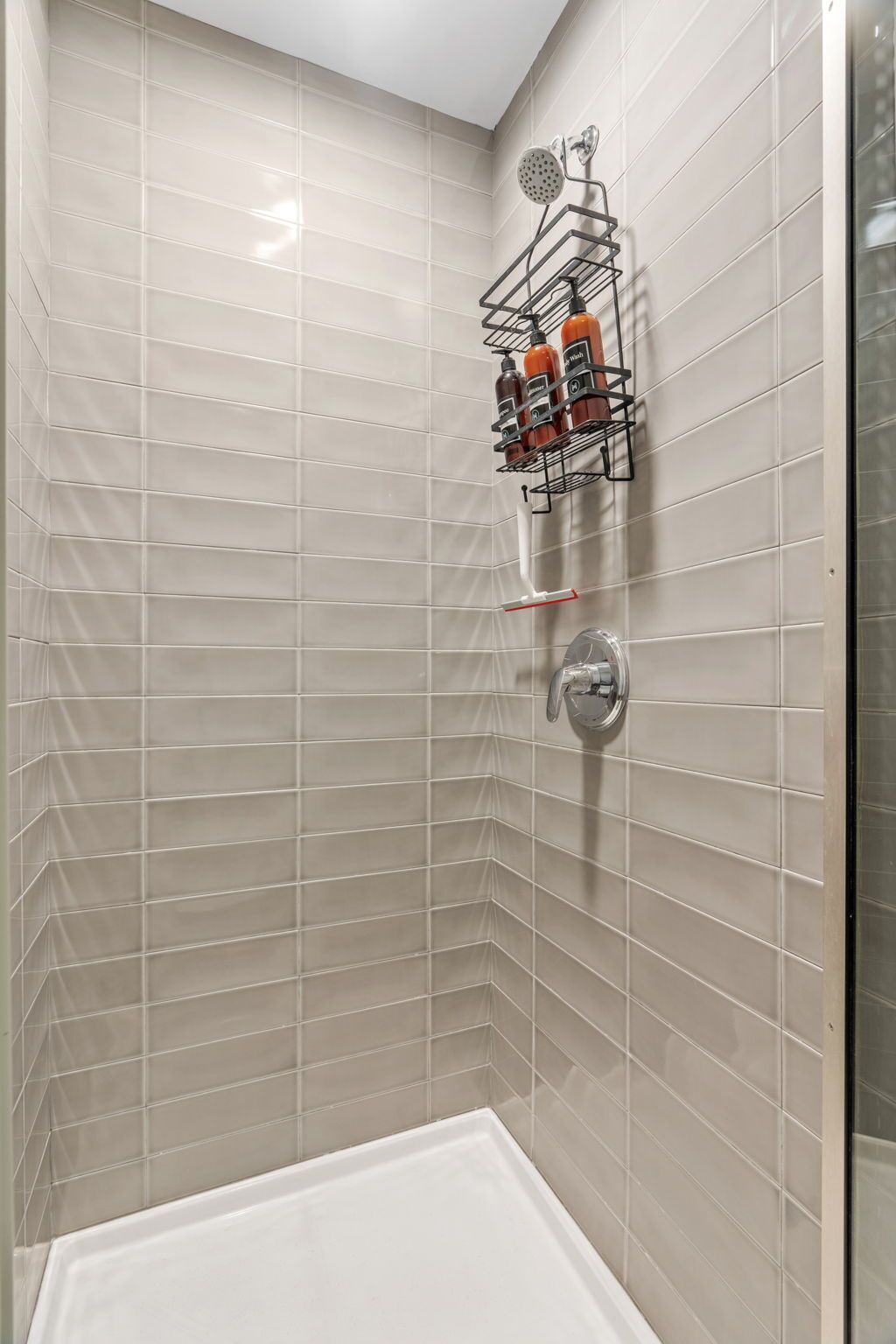 A shower area with beige tiles, a glass shower enclosure, and a metal rack holding toiletries.