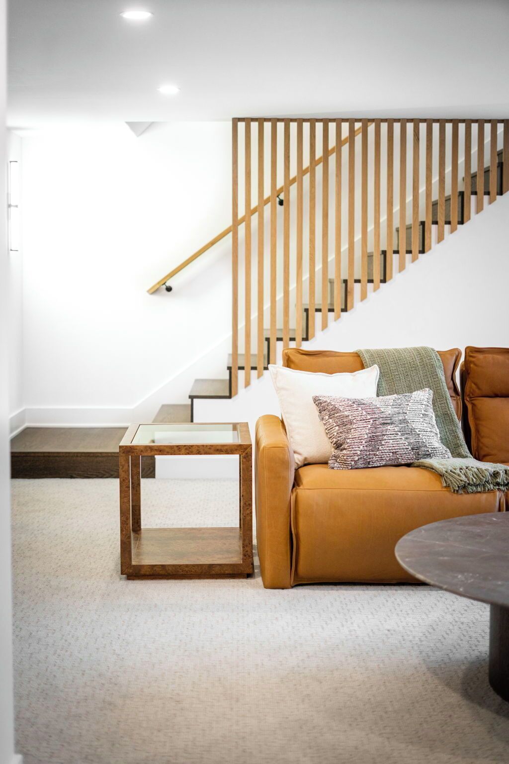 A modern living room with a wooden staircase, a brown leather sofa, and a small wooden coffee table.