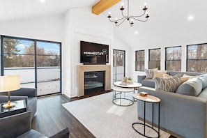 A modern living room with a fireplace, large windows, a sofa, and a television.