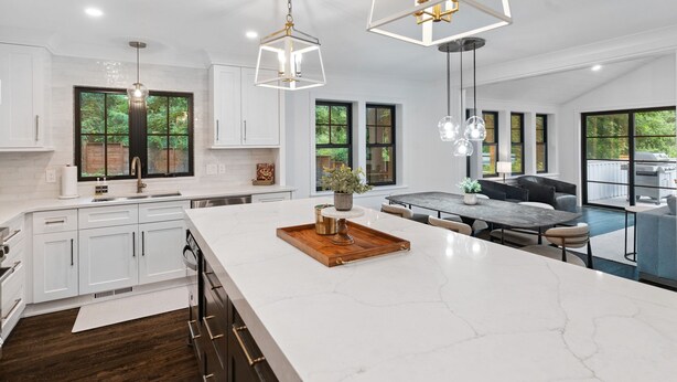 Une cuisine moderne avec des meubles blancs, un grand îlot central et des luminaires suspendus.