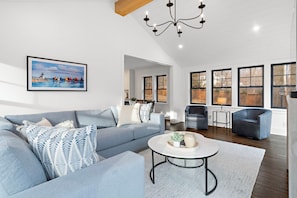 A spacious living room with a grey sofa, a coffee table, and a painting of a coastal scene.