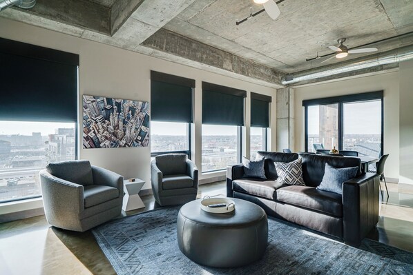Una sala moderna con una amplia vista de la ciudad, un otoman redondo y un sofá modular.