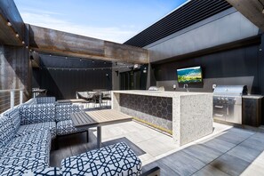 Un patio al aire libre con un área de estar, un bar y una parrilla.
