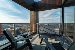 Un balcón con dos sillas y una mesa, con vistas a un paisaje urbano que incluye edificios y una autopista.