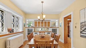 A dining room with a wooden table and chairs, a chandelier, and a view of the kitchen through a window with a radiator. - Pillsbury Hideaway (Minneapolis)