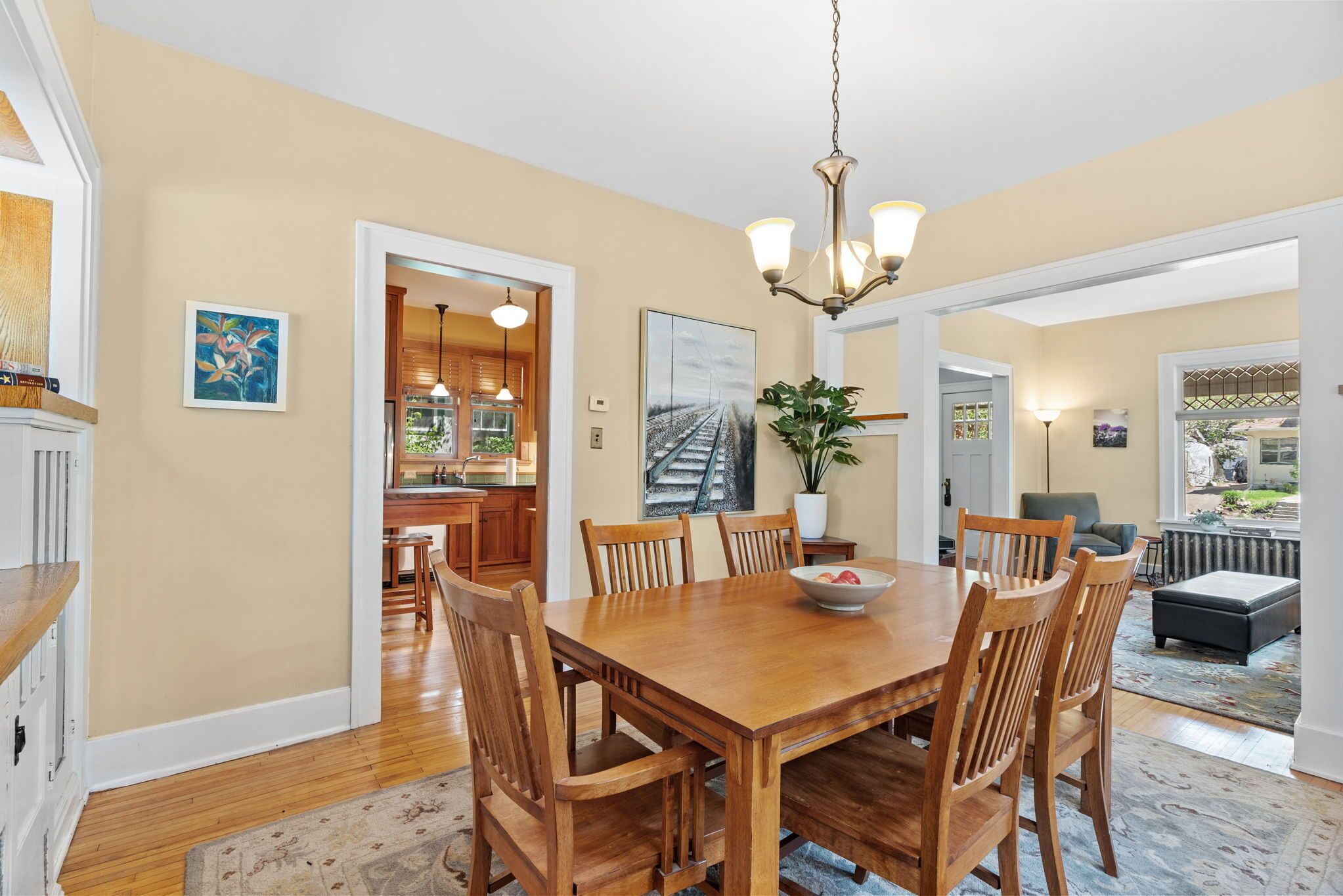 A dining area with a wooden table and chairs, a chandelier, and a view into the kitchen.
