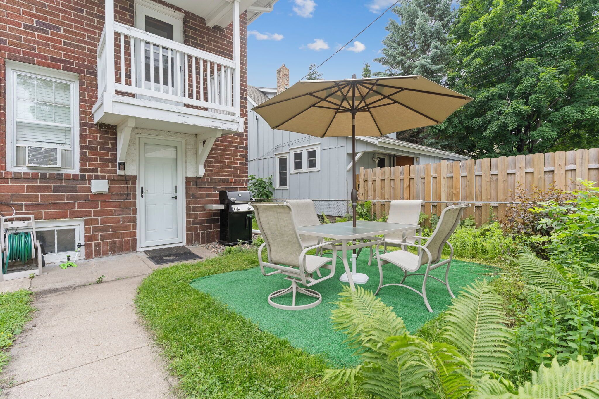 Un jardin avec une table et des chaises de patio, un barbecue et une clôture en bois.