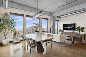 A modern living room with a dining area, large windows, a flat-screen TV, and a city view. - Sable 902 - Penthouse (Minneapolis)