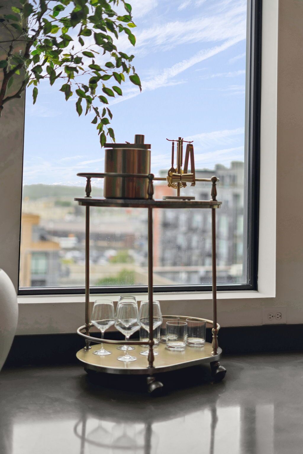 A metal tray table with glasses and a small plant by a window.