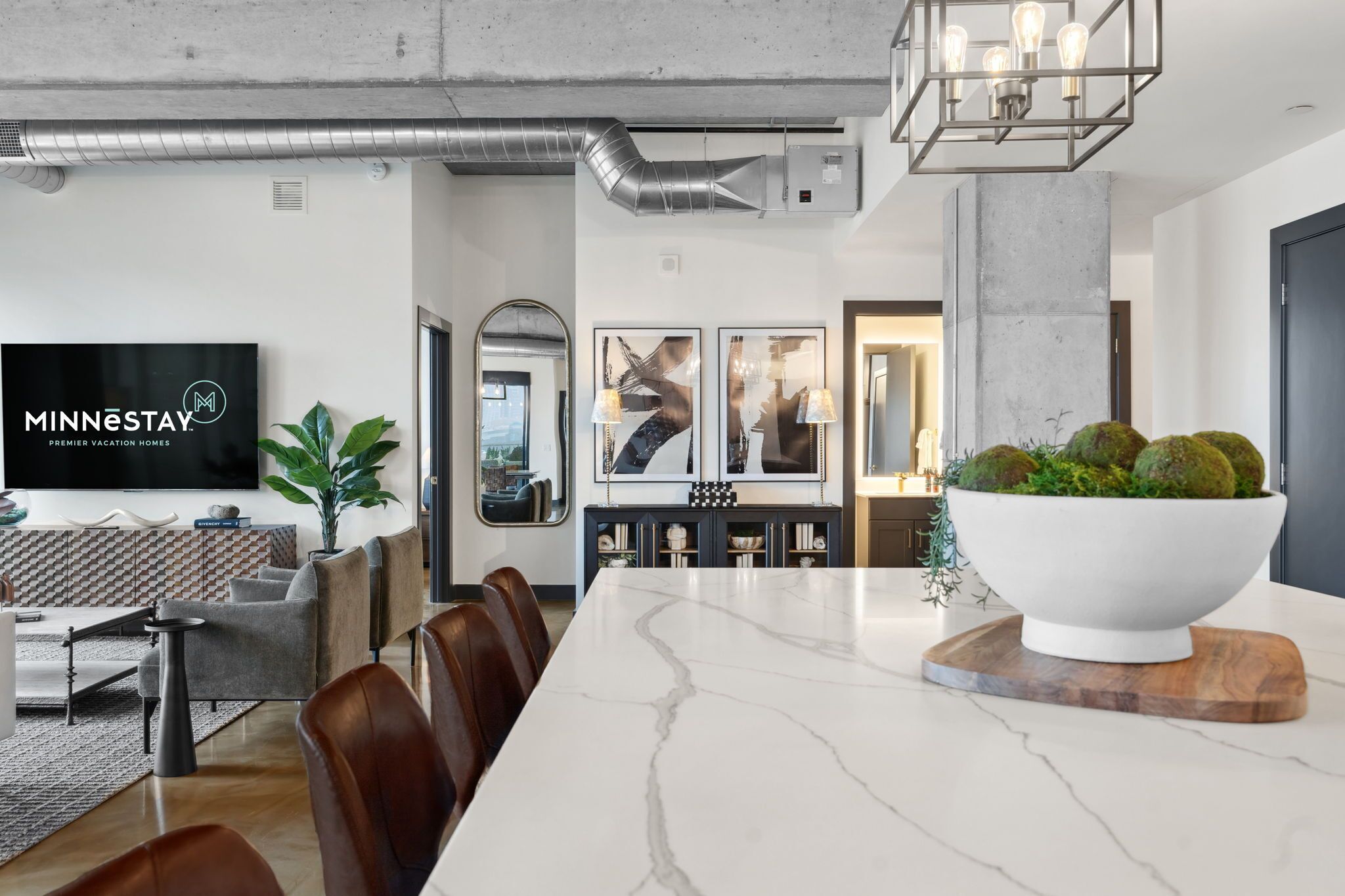 A modern dining area with a marble table, leather chairs, a large white bowl centerpiece, and a television displaying 'MINNESOTAY' branding.