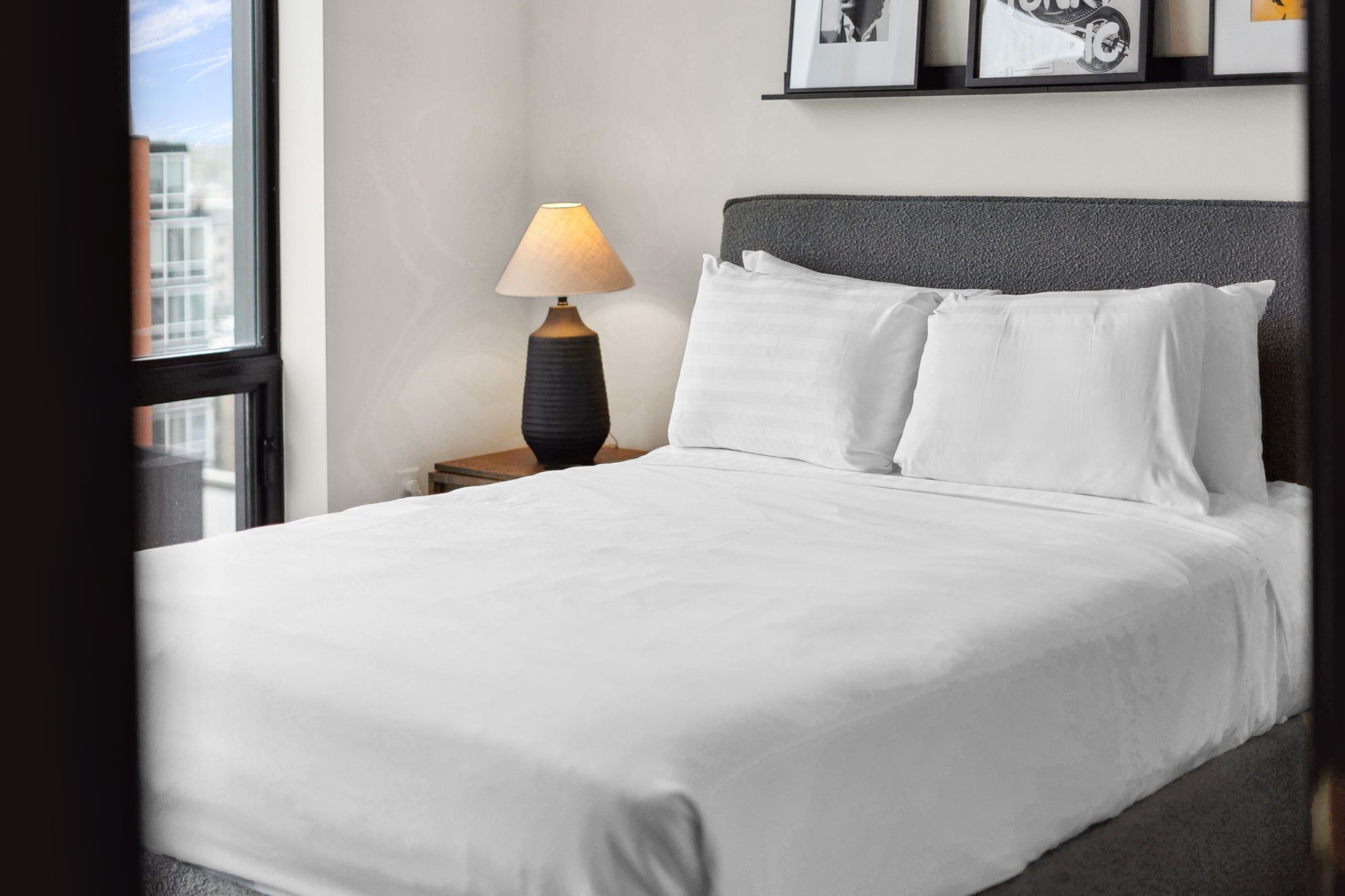 A neatly made bed with white linens, a dark headboard, and a bedside lamp.