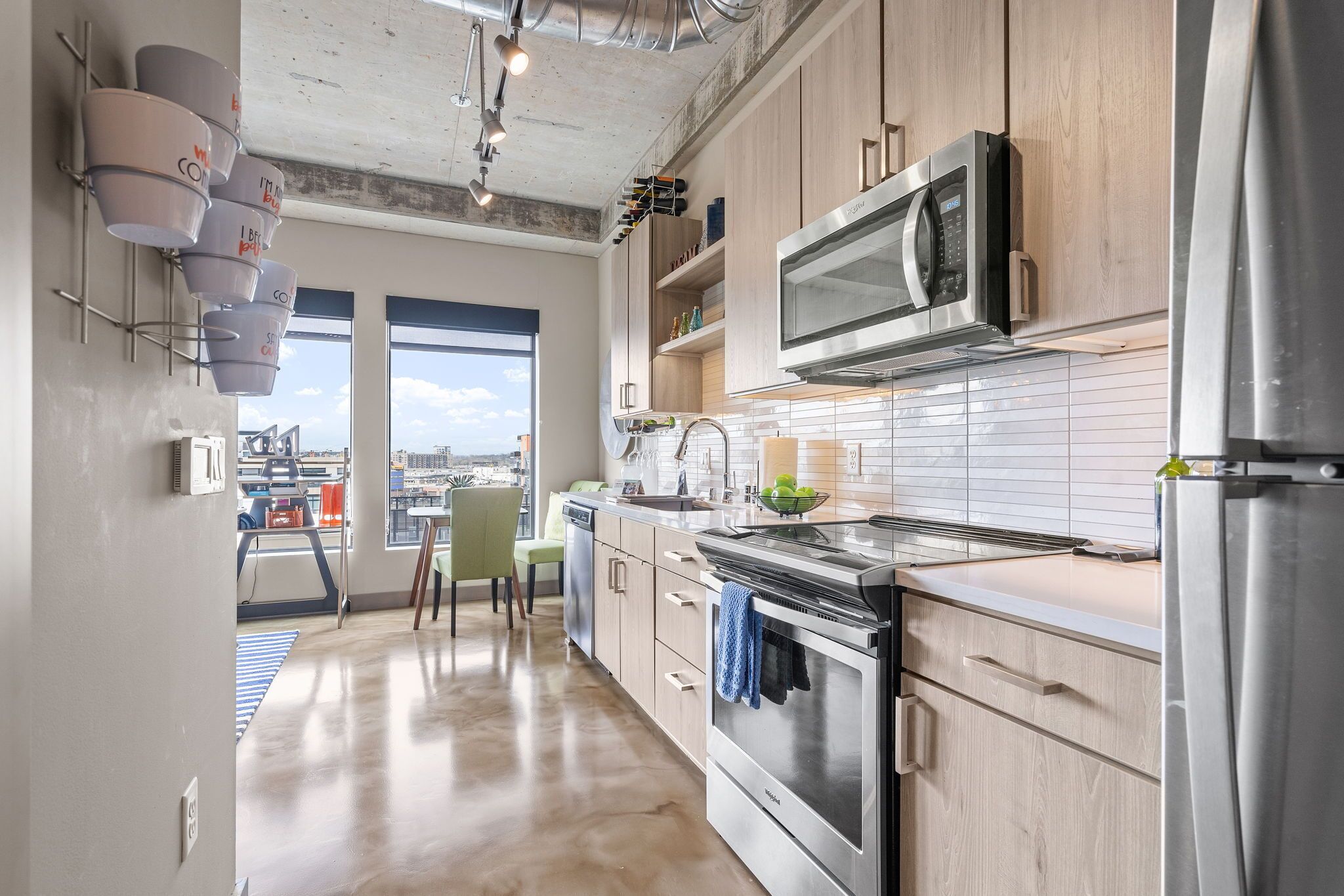 Une cuisine moderne dotée de meubles en bois, d’appareils électroménagers en acier inoxydable et d’une grande fenêtre offrant une vue sur la ville.