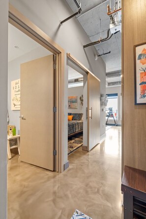A modern interior with a hallway leading to a bedroom, featuring a bed, a nightstand, and a wall-mounted artwork.