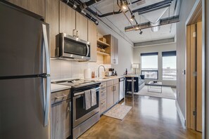 A modern kitchen with stainless steel appliances, wooden cabinets, and a large window offering a city view. - Sable 803 - Alcove (Minneapolis)
