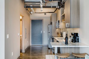 A modern kitchen with stainless steel appliances, a white countertop, and wooden bar stools. - Sable 803 - Alcove (Minneapolis)