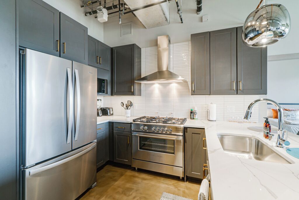 A modern kitchen with stainless steel appliances, grey cabinets, and a white countertop.