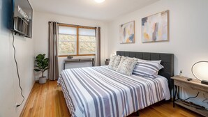 A modern bedroom with a bed, a TV mounted on the wall, and a window with curtains. - D. The Retreat at Linden Hills (Minneapolis)