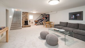 A modern living room with a staircase, a fireplace, a gaming area, and a gray sofa. - D. The Retreat at Linden Hills (Minneapolis)