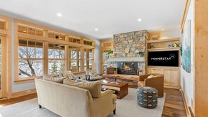 A spacious living room with a stone fireplace, large windows, and a cozy seating area. - Turtle Lake Cottage (Shoreview)