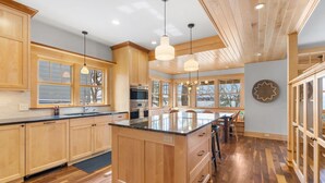 A spacious kitchen with wooden cabinets, a large island, pendant lights, and large windows. - Turtle Lake Cottage (Shoreview)